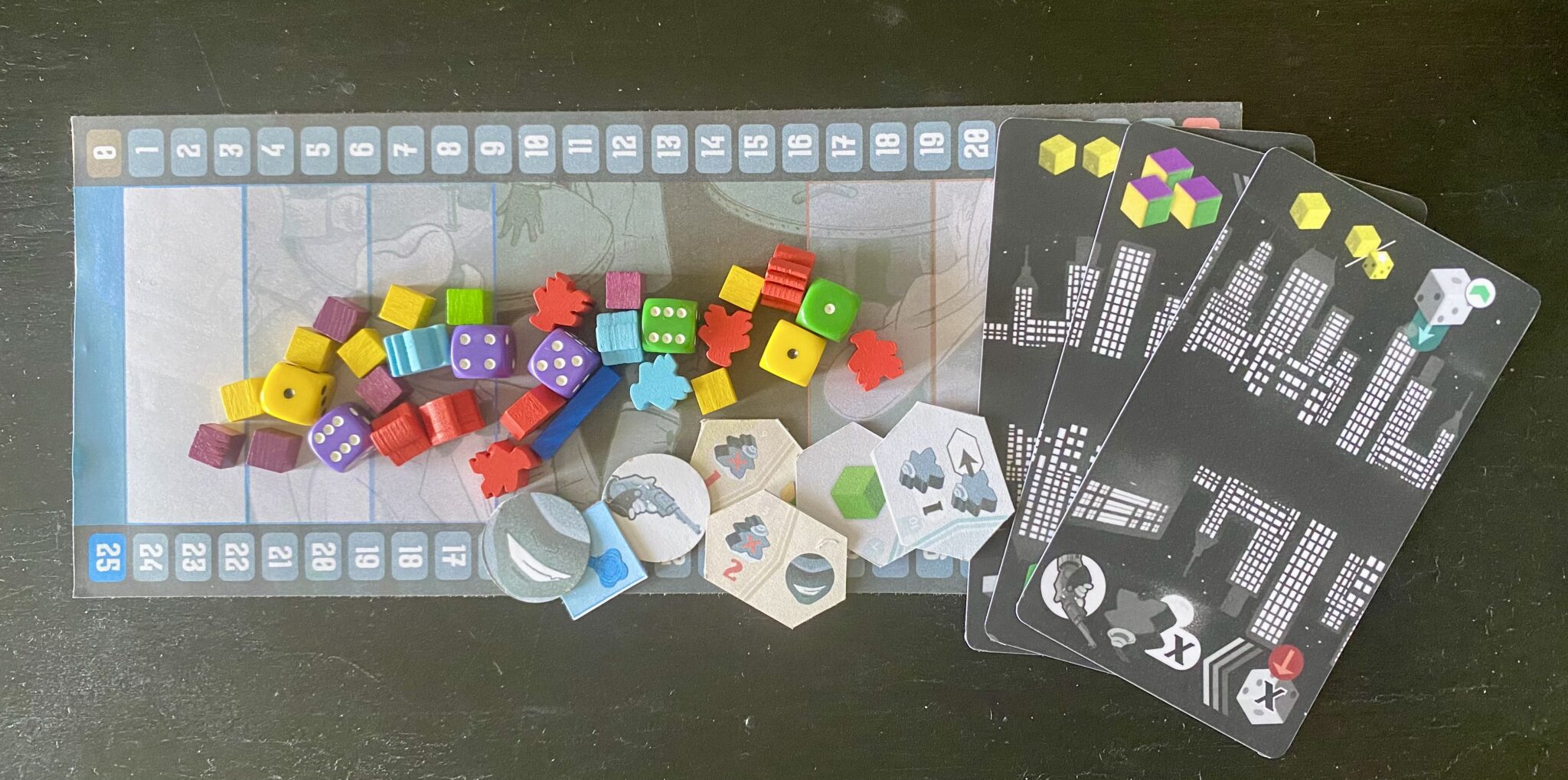 assorted colorful dice and square cubes next to rectangular cards with buildings printed on them, and small pieces from puppets in high places