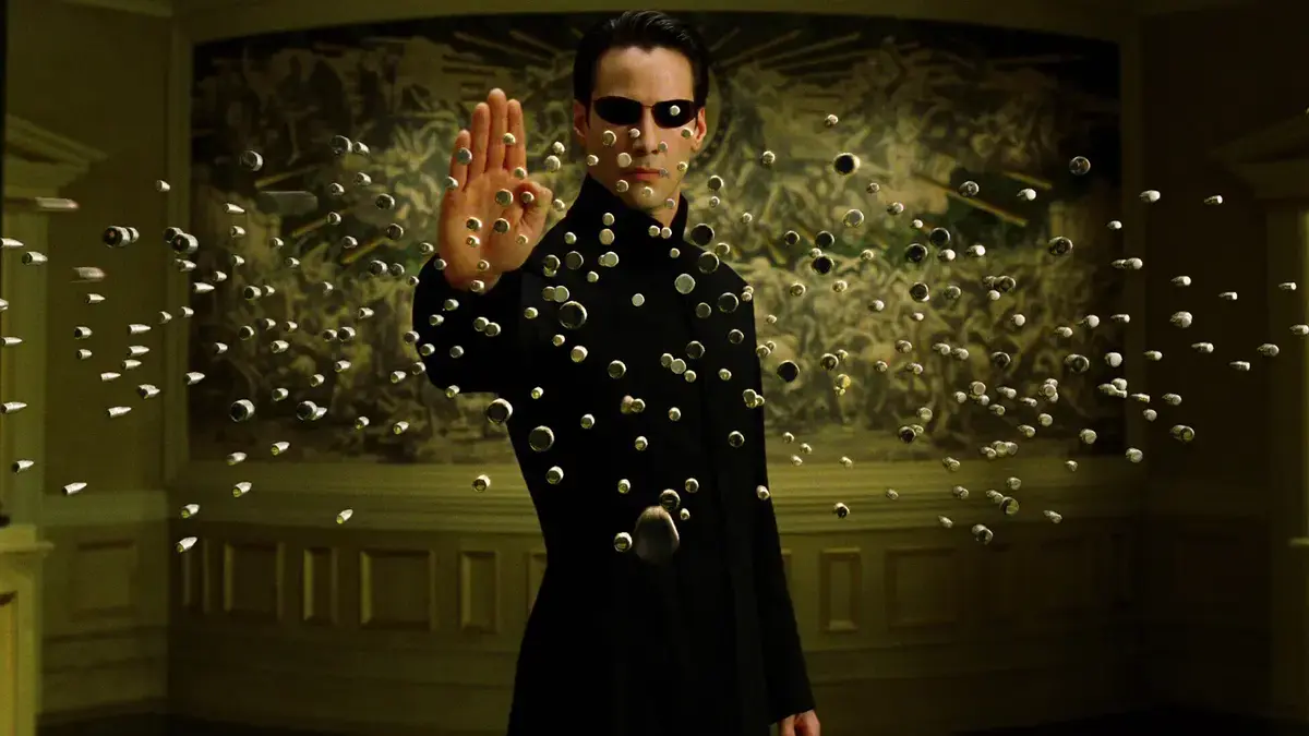 Keanu Reeves as Neo stops bullets coming towards him with his hand. 