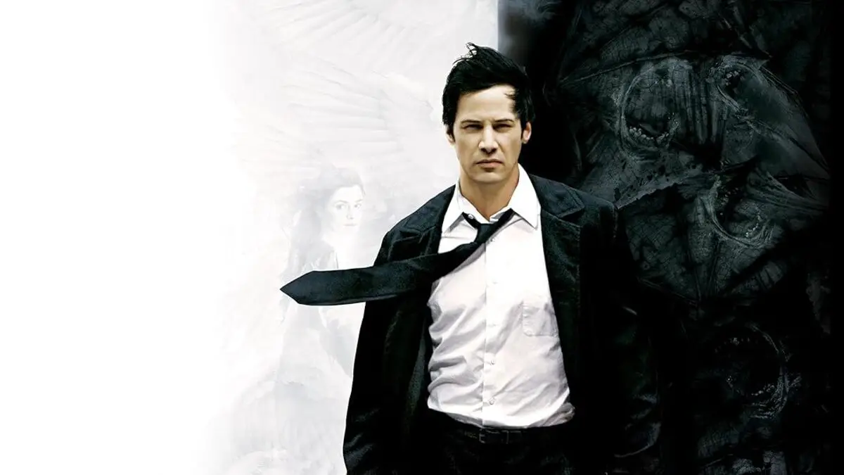 Keanu Reeves as John Constantine walks forward with a half black half white background behind him, with angel and demon imagery. 