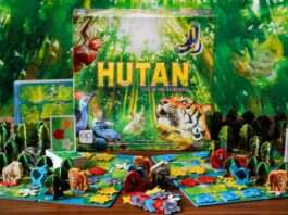 Hutan board game box behind all the components, all are colorful and bright and rainforest themed