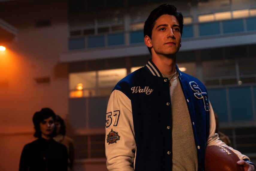 Milo Manheim stands outside with a football, with Sarah Yarkin behind him in the background. 